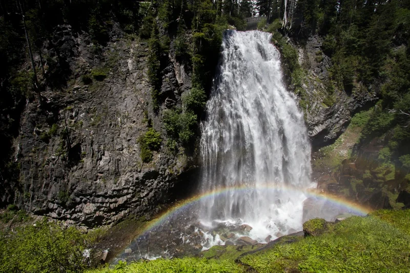 A fan-shaped waterfall cascades over lava cliffs with a rainbow in its mist.